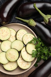 Photo of Slices of fresh eggplants, whole ones and parsley on wooden table, flat lay