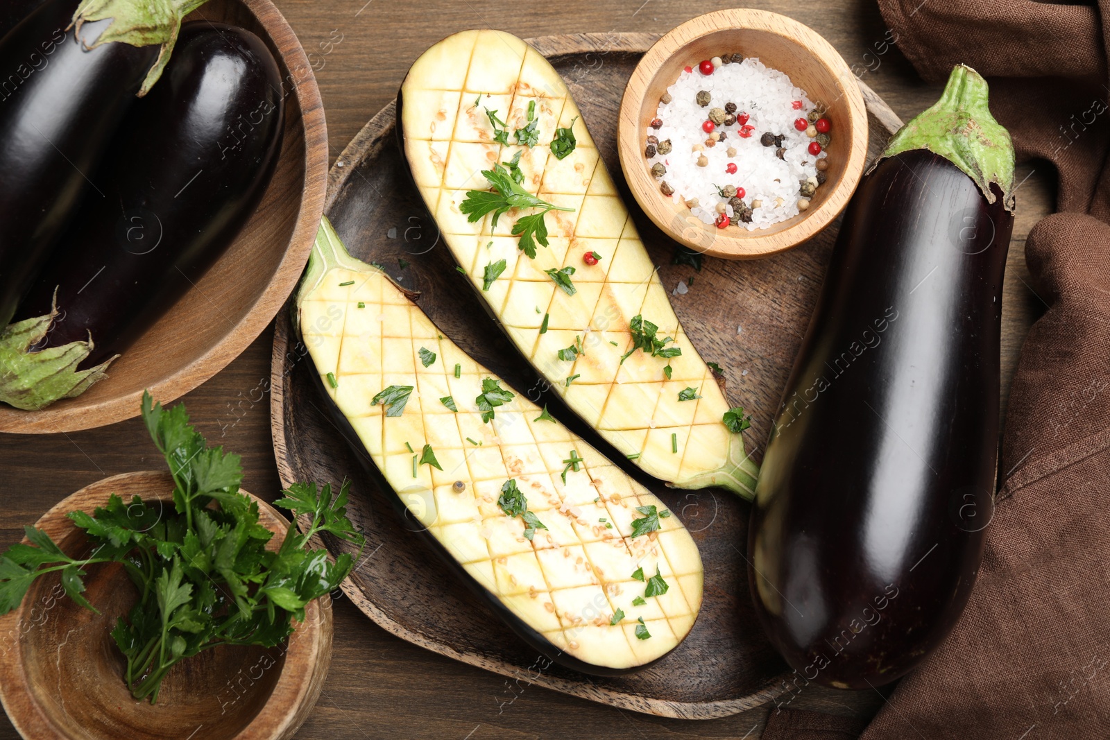 Photo of Halves of fresh eggplant, whole ones, spices and parsley on wooden table, flat lay