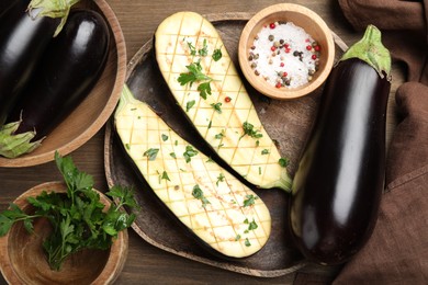 Photo of Halves of fresh eggplant, whole ones, spices and parsley on wooden table, flat lay