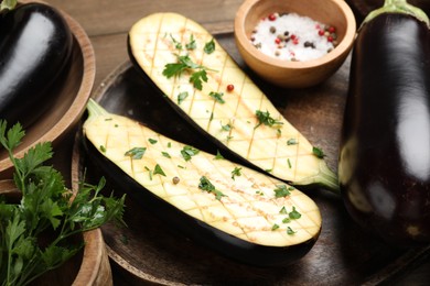 Photo of Halves of fresh eggplant, whole ones, spices and parsley on wooden table, closeup