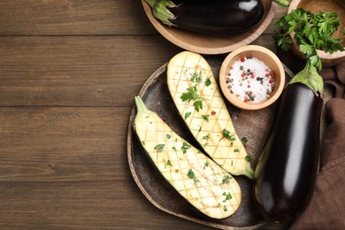 Photo of Halves of fresh eggplant, whole ones, spices and parsley on wooden table, flat lay. Space for text