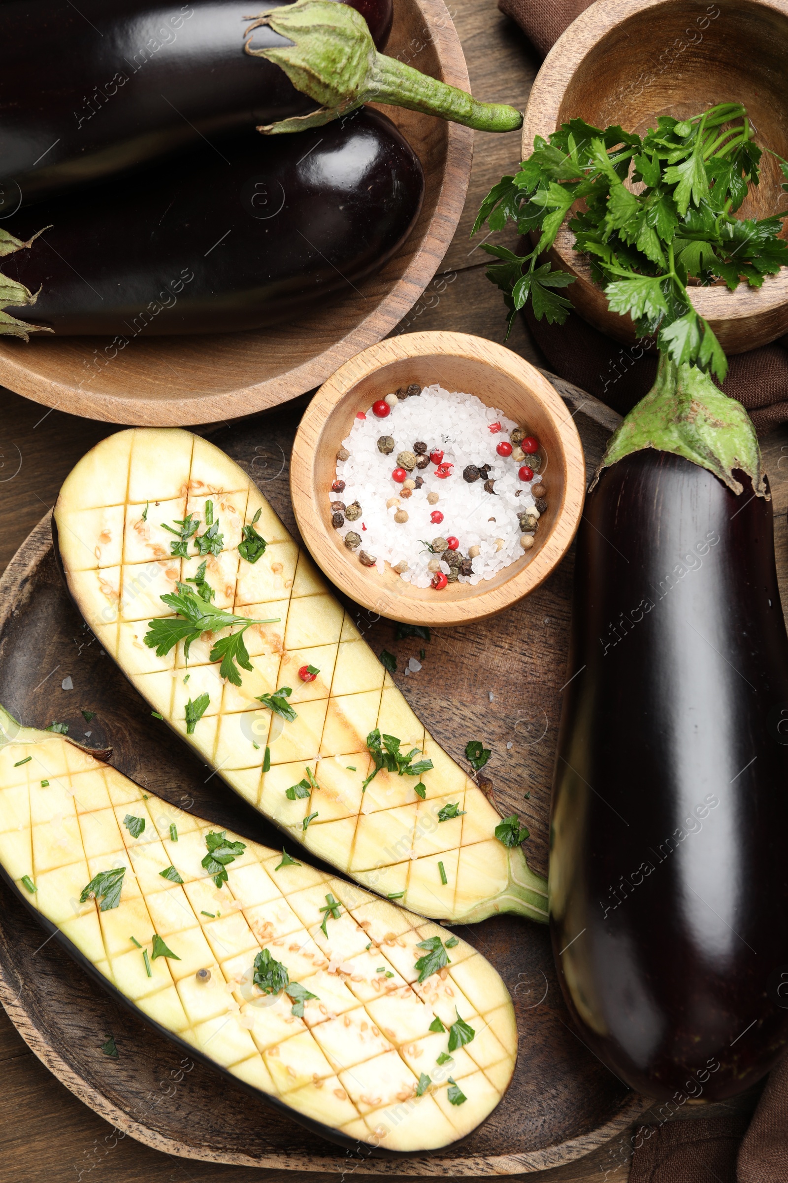 Photo of Halves of fresh eggplant, whole ones, spices and parsley on wooden table, flat lay