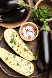 Photo of Halves of fresh eggplant, whole ones, spices and parsley on wooden table, flat lay