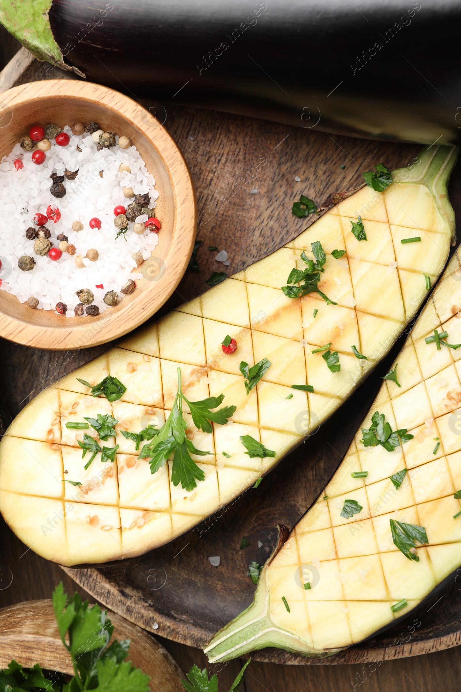 Photo of Halves of fresh eggplant, whole one, spices and parsley on wooden table, flat lay