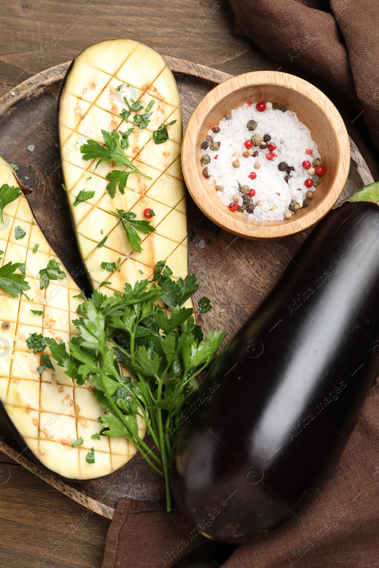 Photo of Halves of fresh eggplant, whole one, spices and parsley on wooden table, flat lay