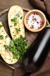 Photo of Halves of fresh eggplant, whole one, spices and parsley on wooden table, flat lay