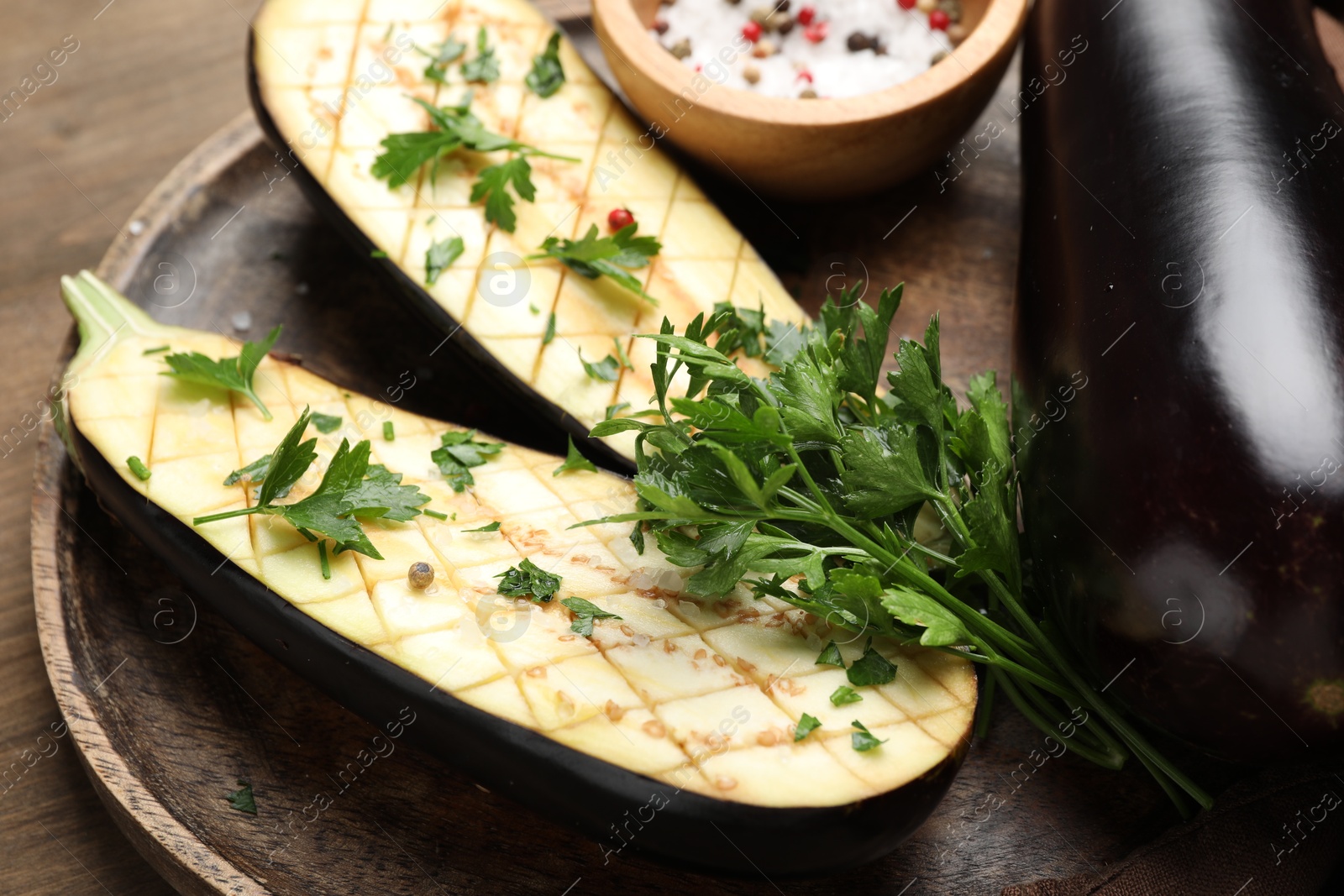 Photo of Halves of fresh eggplant, whole one, spices and parsley on wooden table, closeup