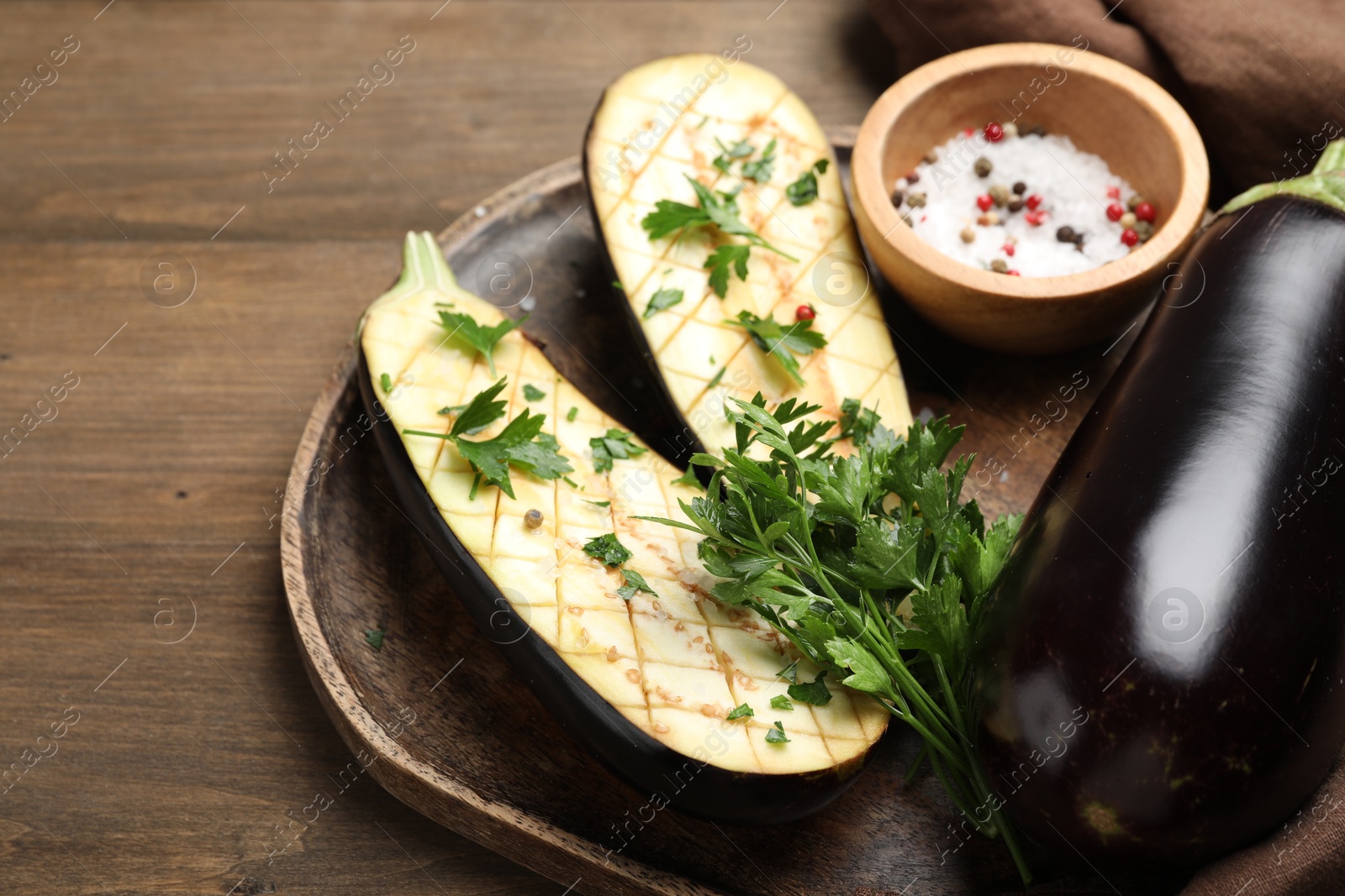 Photo of Halves of fresh eggplant, whole one, spices and parsley on wooden table, closeup