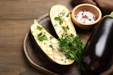 Photo of Halves of fresh eggplant, whole one, spices and parsley on wooden table, closeup