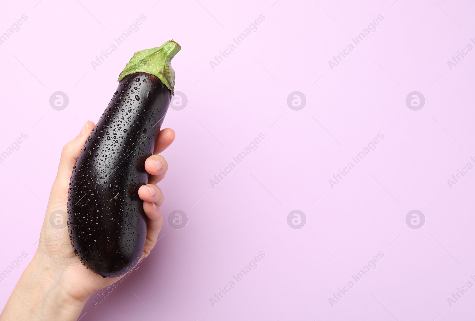 Photo of Woman with fresh wet eggplant on violet background, top view. Space for text