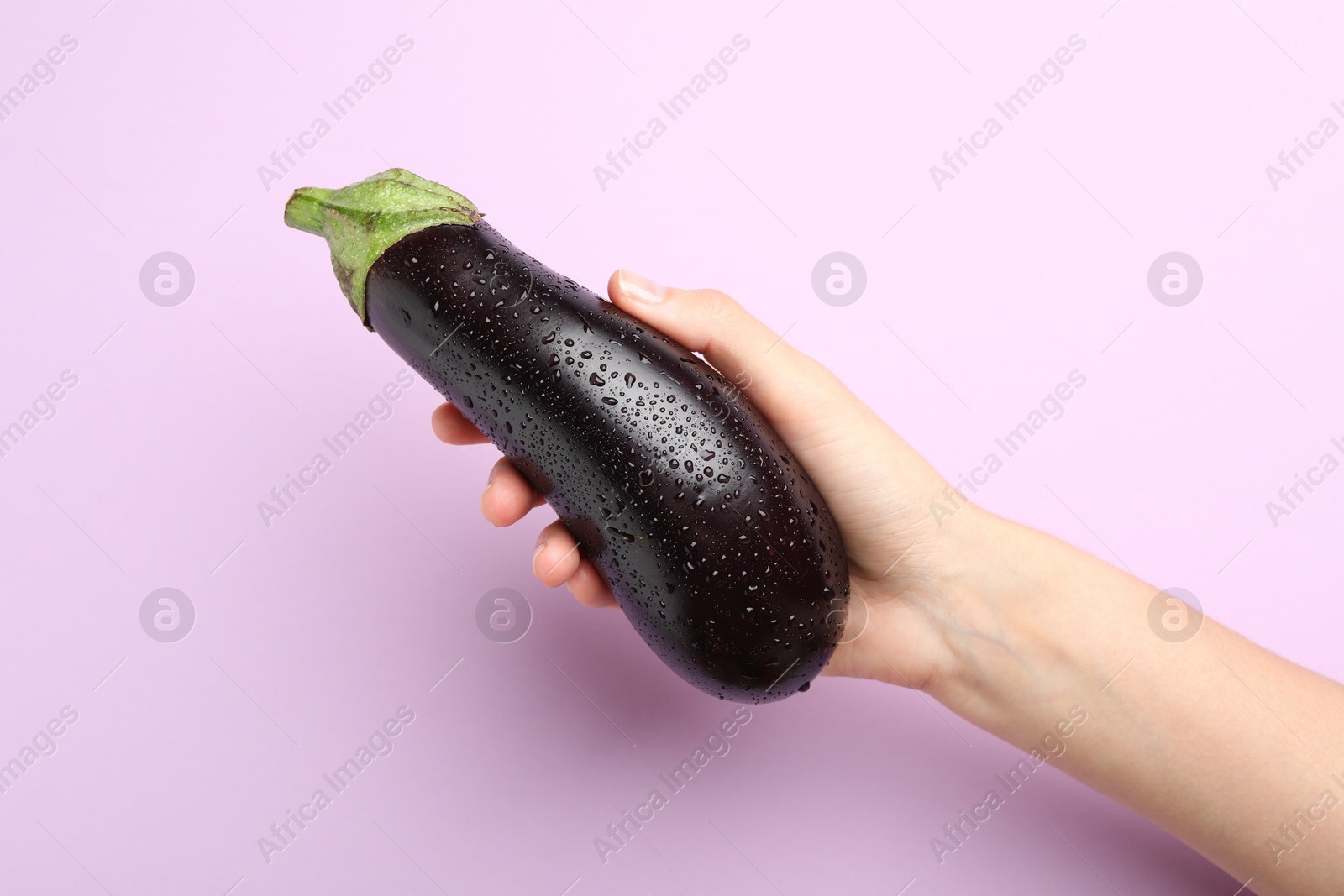 Photo of Woman with fresh wet eggplant on violet background, closeup