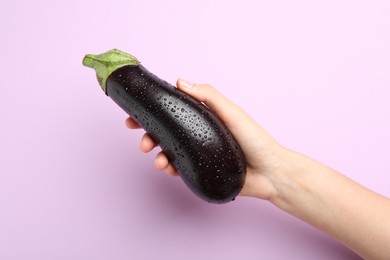 Photo of Woman with fresh wet eggplant on violet background, closeup