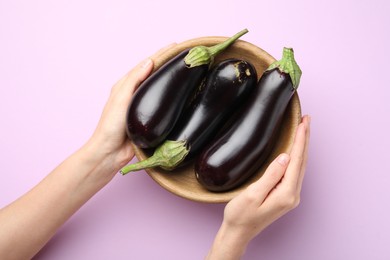 Photo of Woman with bowl of fresh eggplants on violet background, top view