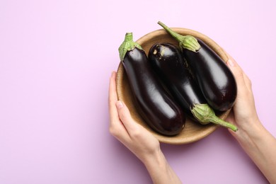 Photo of Woman with bowl of fresh eggplants on violet background, top view. Space for text