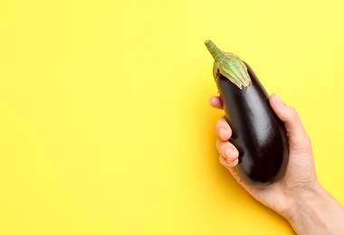 Photo of Woman with fresh eggplant on yellow background, top view. Space for text