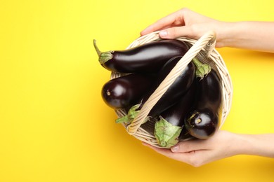 Photo of Woman with wicker basket of fresh eggplants on yellow background, top view. Space for text