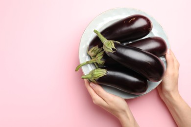 Photo of Woman with plate of fresh eggplants on pink background, top view. Space for text