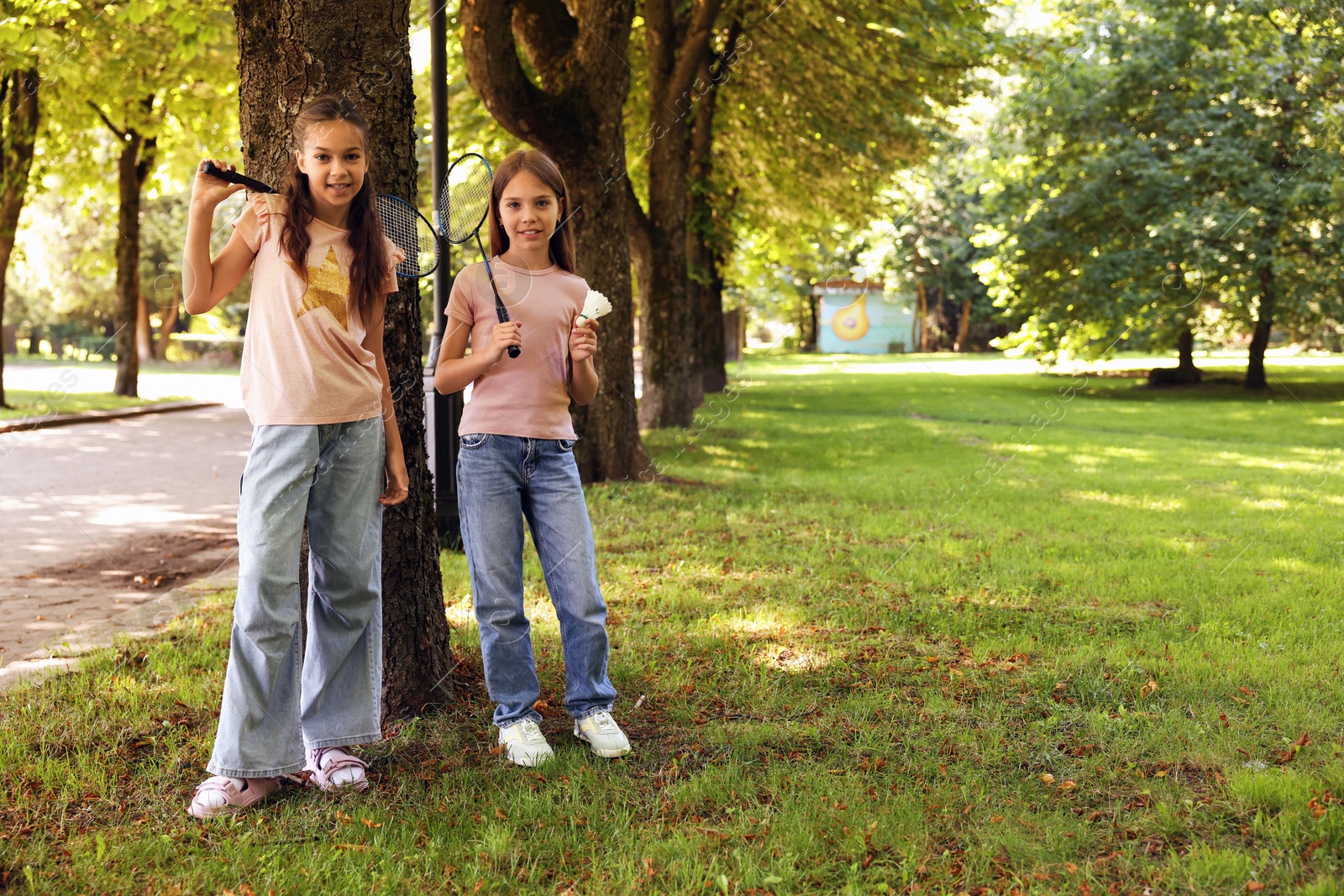 Smiling little girls with badminton rackets and shuttlecock near tree in park. Space for text Photo of Smiling little girls with badminton rackets and shuttlecock near tree in park. Space for text