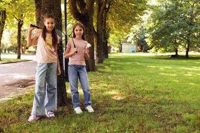 Photo of Smiling little girls with badminton rackets and shuttlecock near tree in park. Space for text