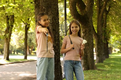 Photo of Smiling little girls with badminton rackets and shuttlecock near tree in park