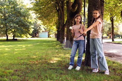 Photo of Smiling little girls with badminton rackets and shuttlecock near tree in park. Space for text