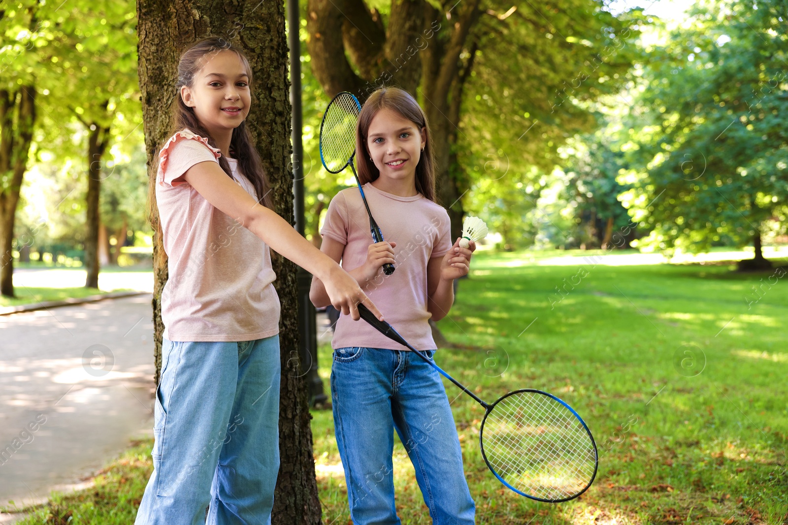 Smiling little girls with badminton rackets and shuttlecock near tree in park Photo of Smiling little girls with badminton rackets and shuttlecock near tree in park