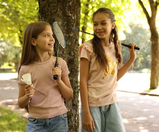 Photo of Smiling little girls with badminton rackets and shuttlecock near tree in park