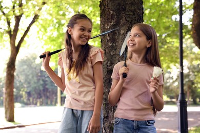 Photo of Smiling little girls with badminton rackets and shuttlecock near tree in park