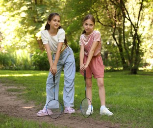 Photo of Cute little girls with badminton rackets posing in park