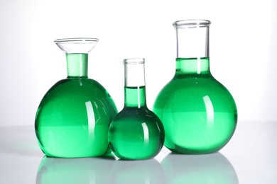 Photo of Different laboratory glassware with green liquid on mirror surface against white background