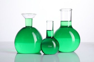 Photo of Different laboratory glassware with green liquid on mirror surface against white background