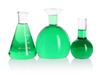 Photo of Different laboratory glassware with green liquid on mirror surface isolated on white