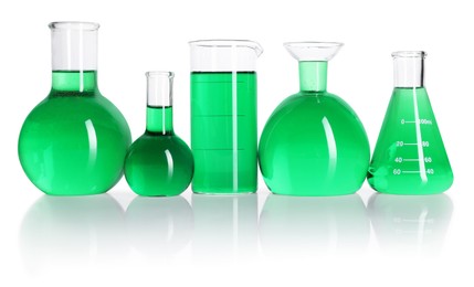 Photo of Different laboratory glassware with green liquid on mirror surface isolated on white