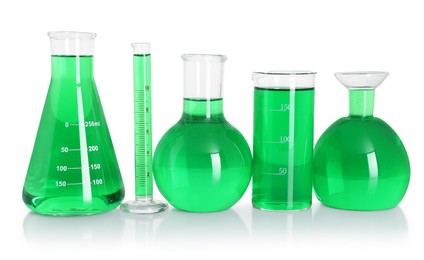 Photo of Different laboratory glassware with green liquid on mirror surface isolated on white