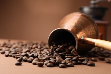 Photo of Cezve and roasted coffee beans on brown background, closeup. Space for text