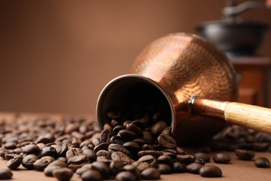 Photo of Cezve and roasted coffee beans on brown background, closeup