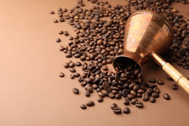 Photo of Cezve and roasted coffee beans on brown background, space for text