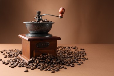 Photo of Coffee grinder and beans on brown background, space for text