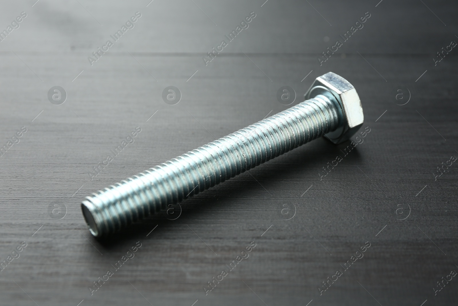 One metal bolt on dark wooden table, closeup Photo of One metal bolt on dark wooden table, closeup