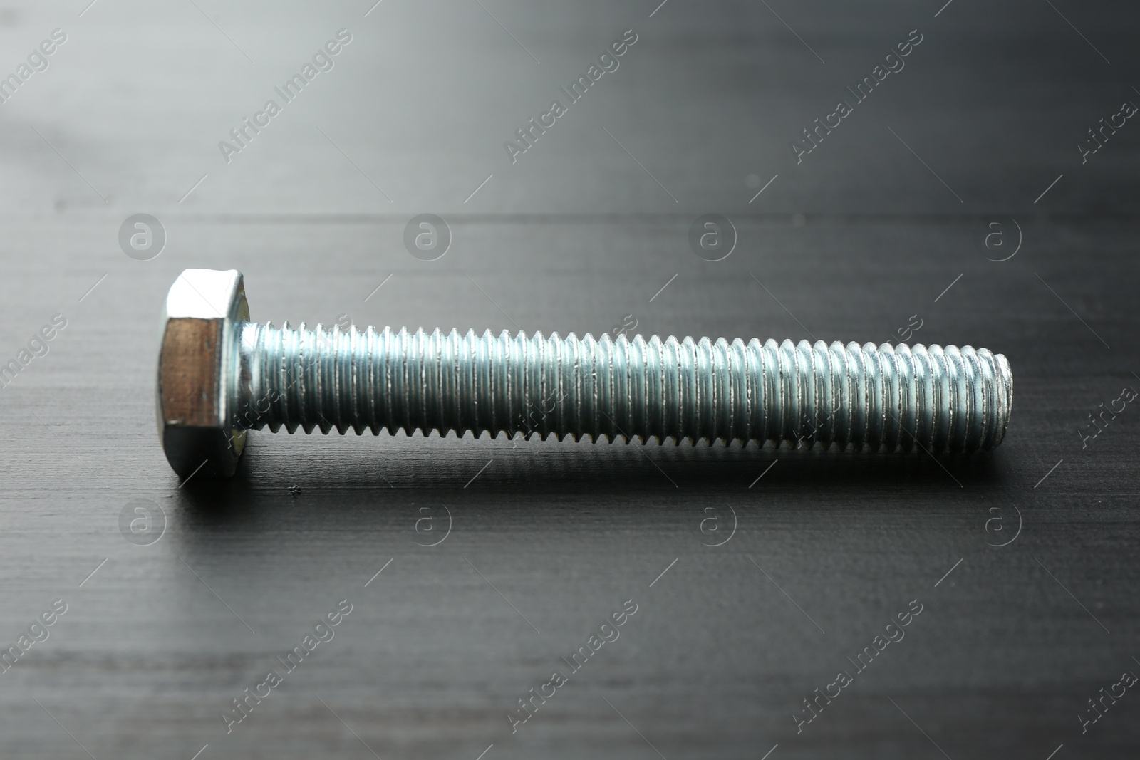 One metal bolt on dark wooden table, closeup Photo of One metal bolt on dark wooden table, closeup