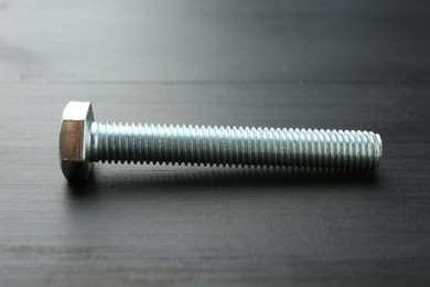 Photo of One metal bolt on dark wooden table, closeup