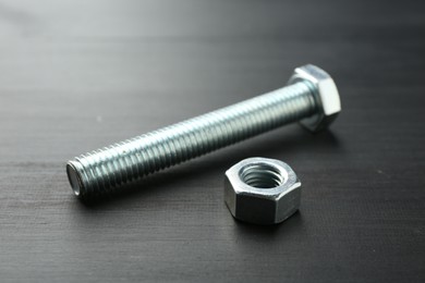 Photo of One metal bolt and hex nut on dark wooden table, closeup