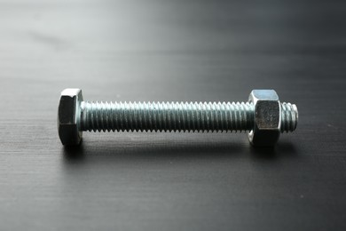 Photo of One metal bolt on dark wooden table, closeup
