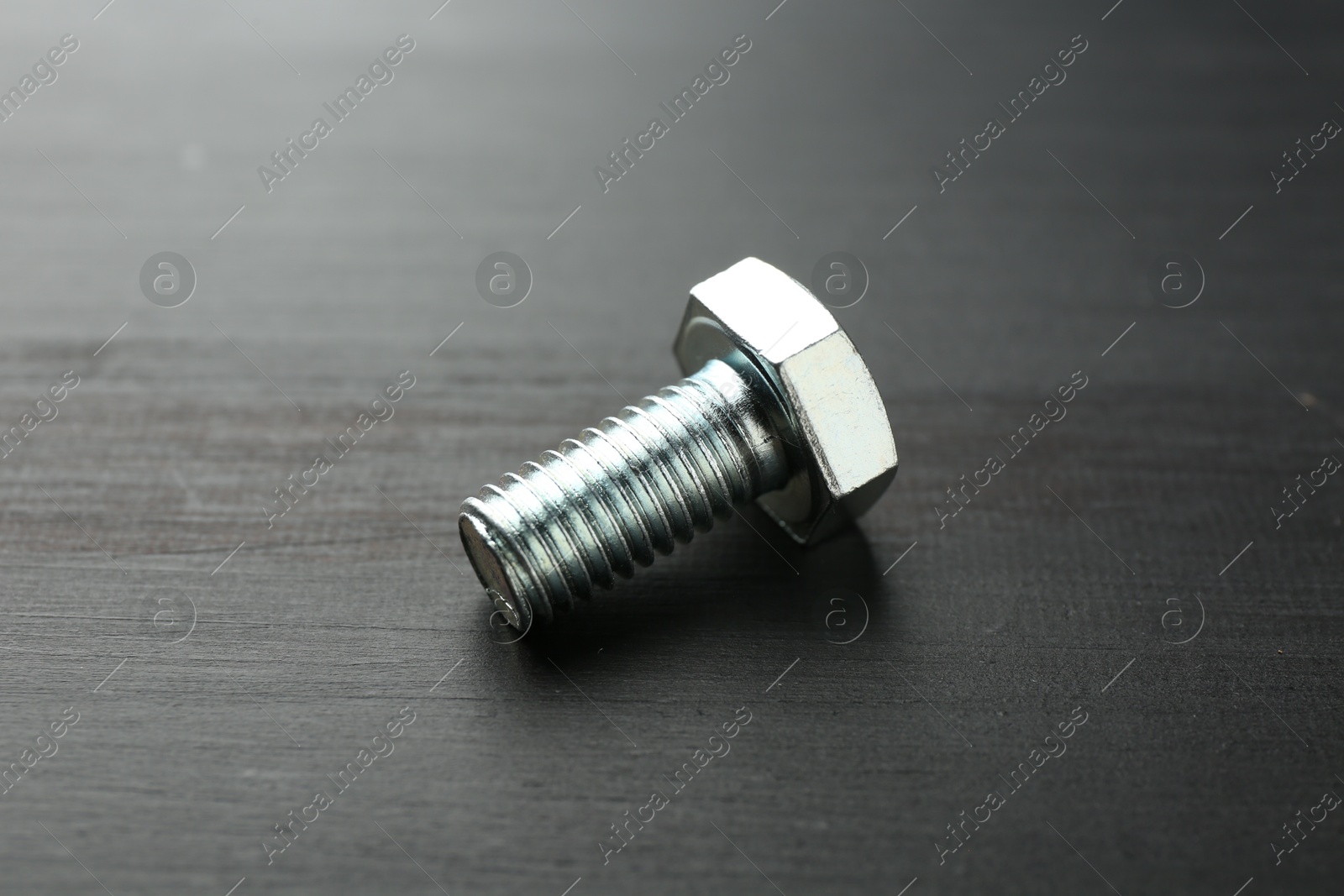 One metal bolt on dark wooden table, closeup Photo of One metal bolt on dark wooden table, closeup