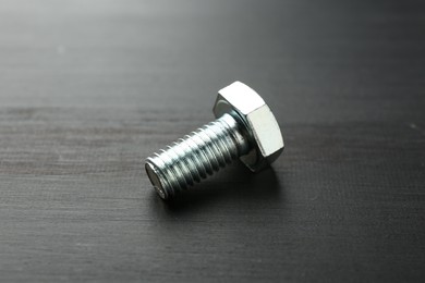 Photo of One metal bolt on dark wooden table, closeup