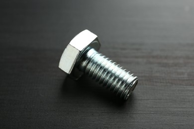 Photo of One metal bolt on dark wooden table, closeup