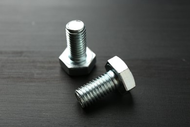Photo of Metal bolts on dark wooden table, closeup