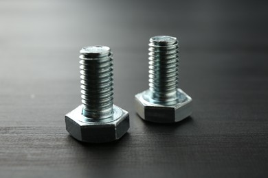 Photo of Metal bolts on dark wooden table, closeup