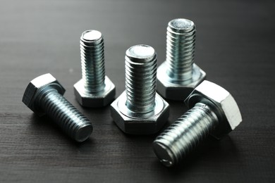 Photo of Metal bolts on dark wooden table, closeup