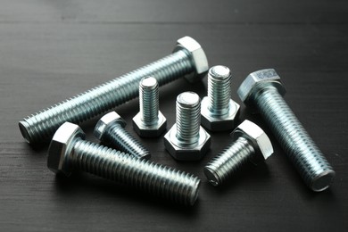 Photo of Metal bolts on dark wooden table, closeup